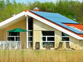 Une maison avec un toit en pente, des panneaux solaires et un espace extérieur clôturé.