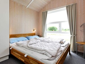 Un lit simple avec une tête de lit en bois, une table de chevet avec une lampe et une fenêtre avec des rideaux.