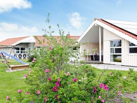 A residential property with a covered patio, a slide, and a garden with pink flowers.