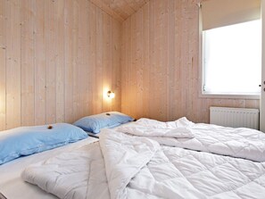 A room with wooden panel walls, a bed with white bedding, a blue pillow, and a wall-mounted light fixture. - Holiday Home in Otterndorf (Otterndorf)
