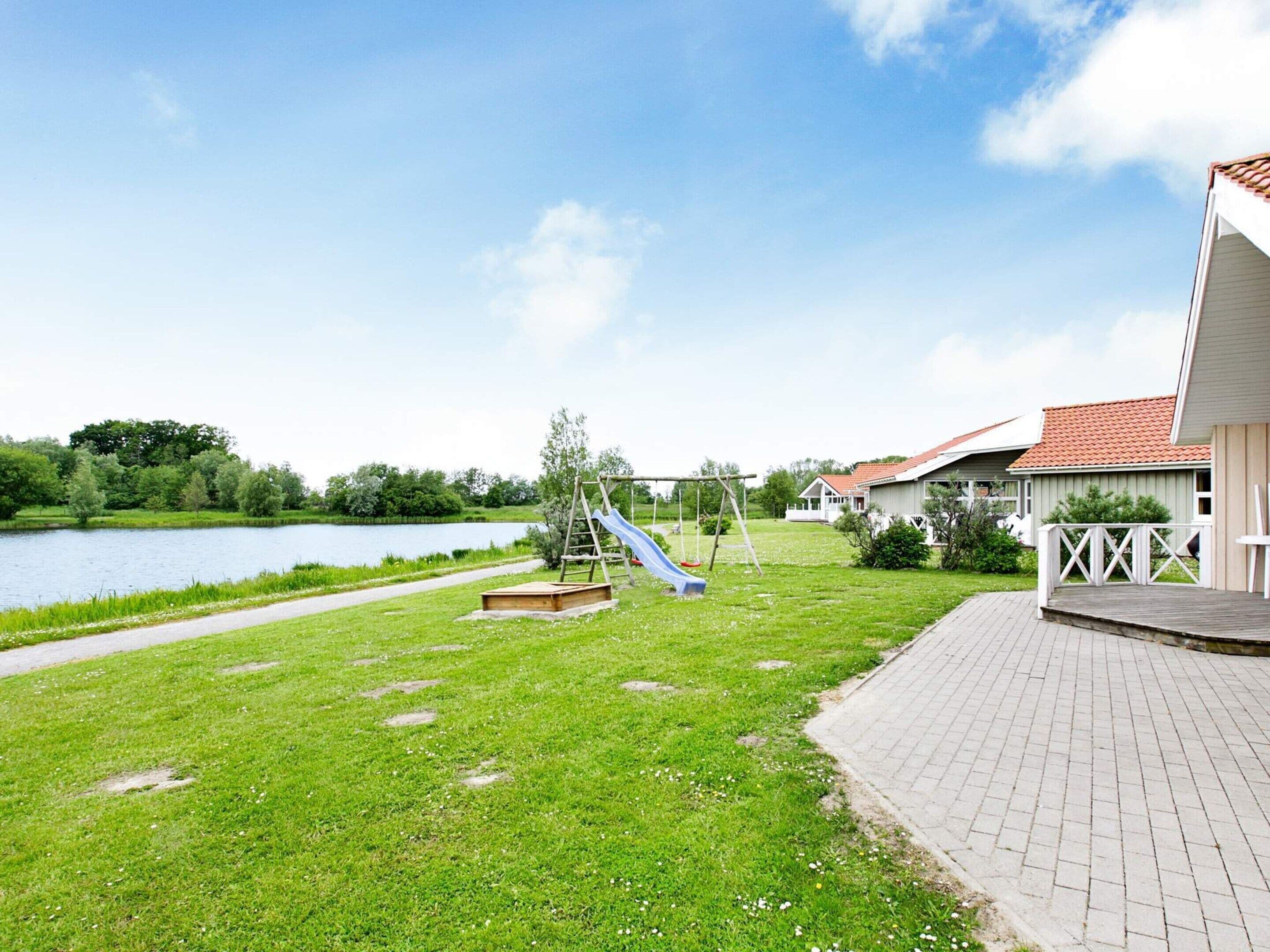 A grassy outdoor area with a playground, a paved path, and a body of water.