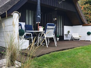 Eine Terrasse mit Tisch und Stühlen, ein kleiner weißer Tisch mit einer Pflanze und ein weißer Stuhl.