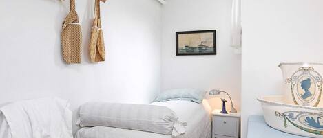 Un dormitorio con una cama, una mesita de noche, una lámpara, un sombrero y un cuadro en la pared.