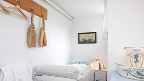 A bedroom with a bed, a nightstand, a lamp, a hat, and a wall-mounted shelf with a decorative item. - Peaceful Holiday Home in Skagen near Sea (Skagen)