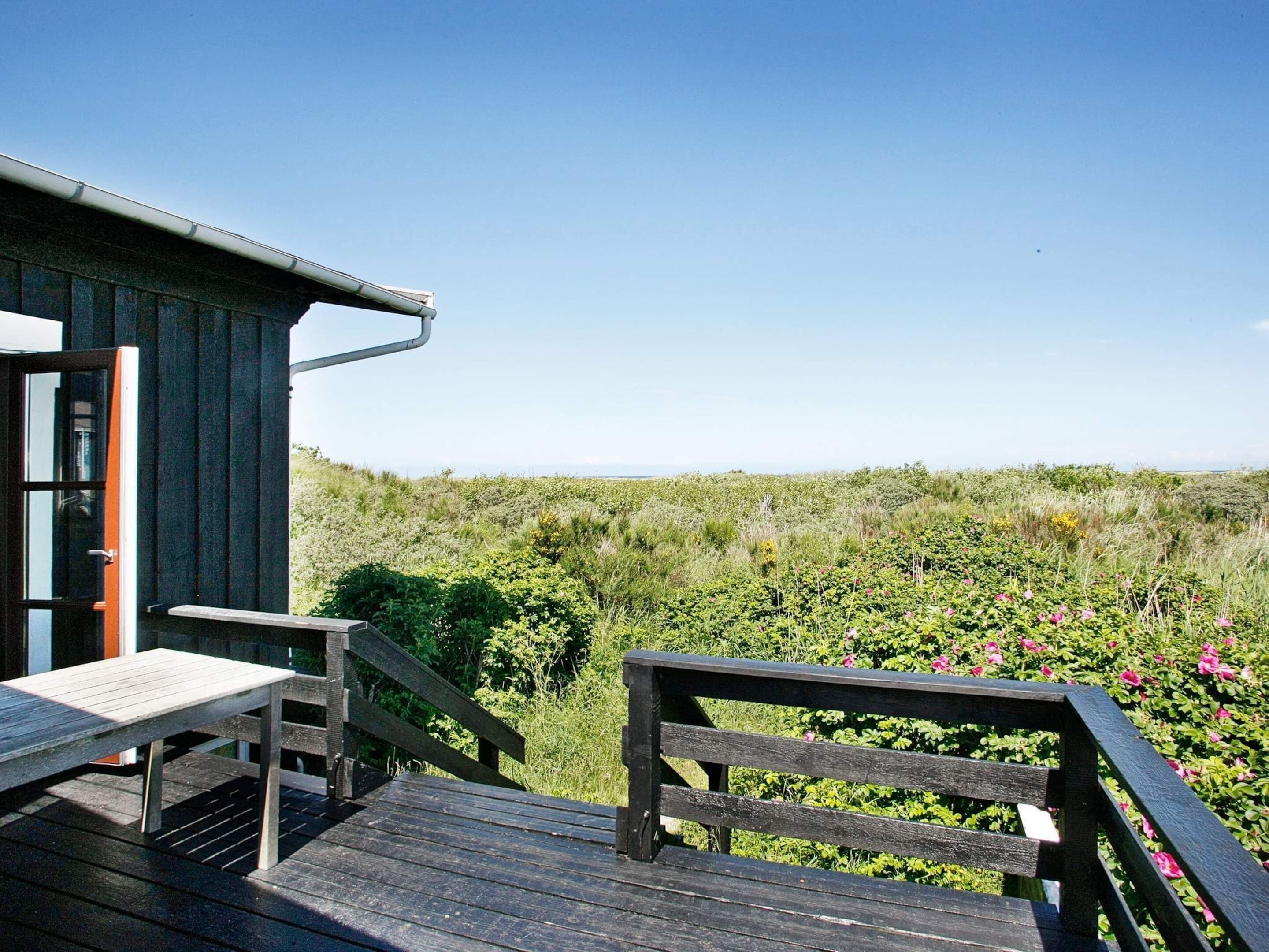Une terrasse en bois avec un banc et une table, offrant une vue sur un paysage naturel caractérisé par une végétation luxuriante et un ciel dégagé.
