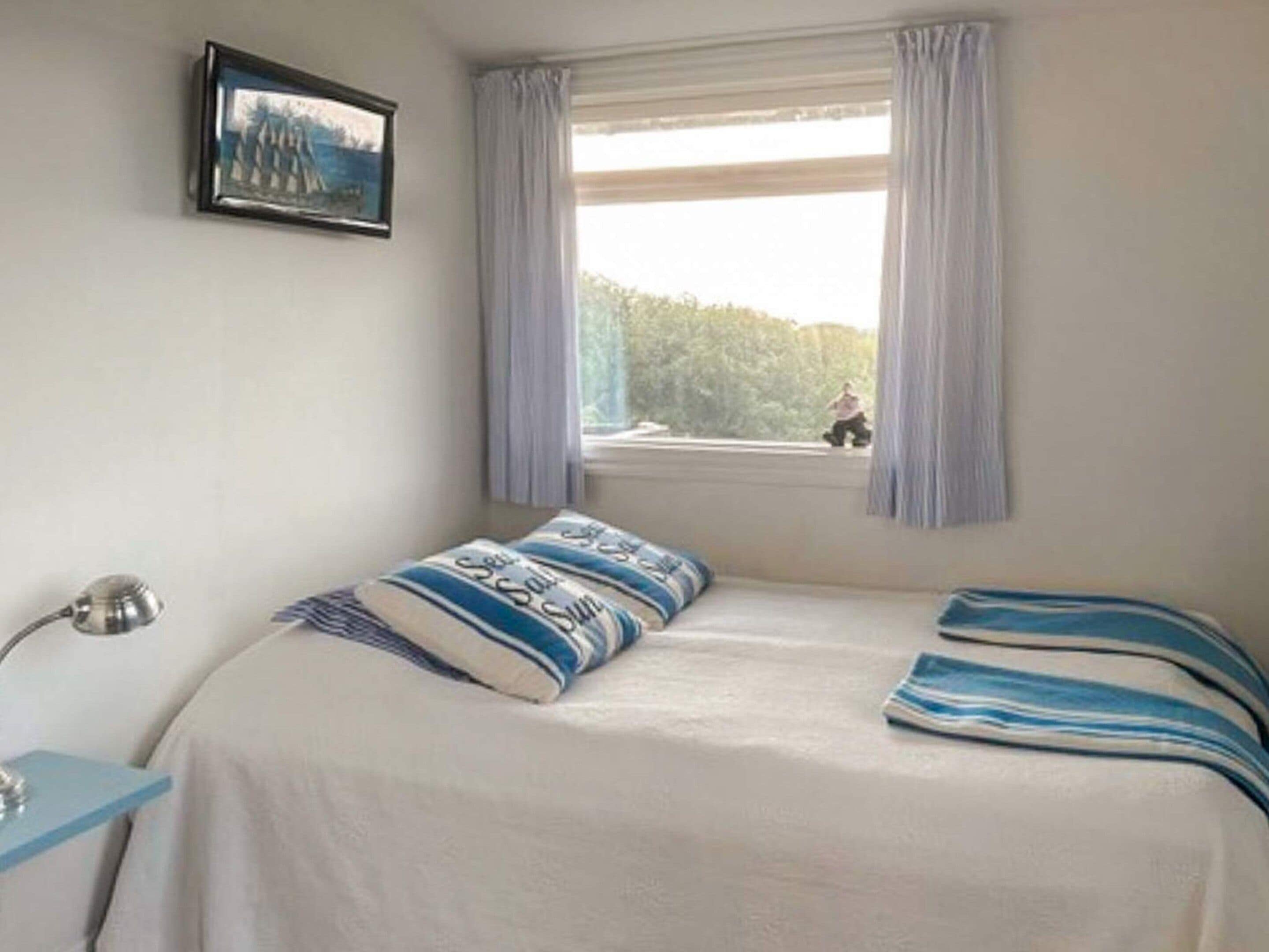 A bedroom with a bed, a window with curtains, a bedside table, and a wall-mounted picture.