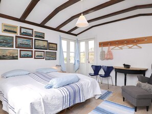 A bedroom with a bed, two chairs, a table, and a hanging coat rack.