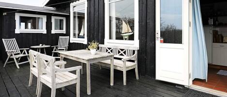 Una terraza de madera con una mesa, sillas, una decoración con forma de velero y una puerta que da a una cocina.
