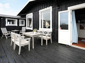 A wooden deck with a table and chairs, a sailboat decoration, and a door leading to a kitchen area.