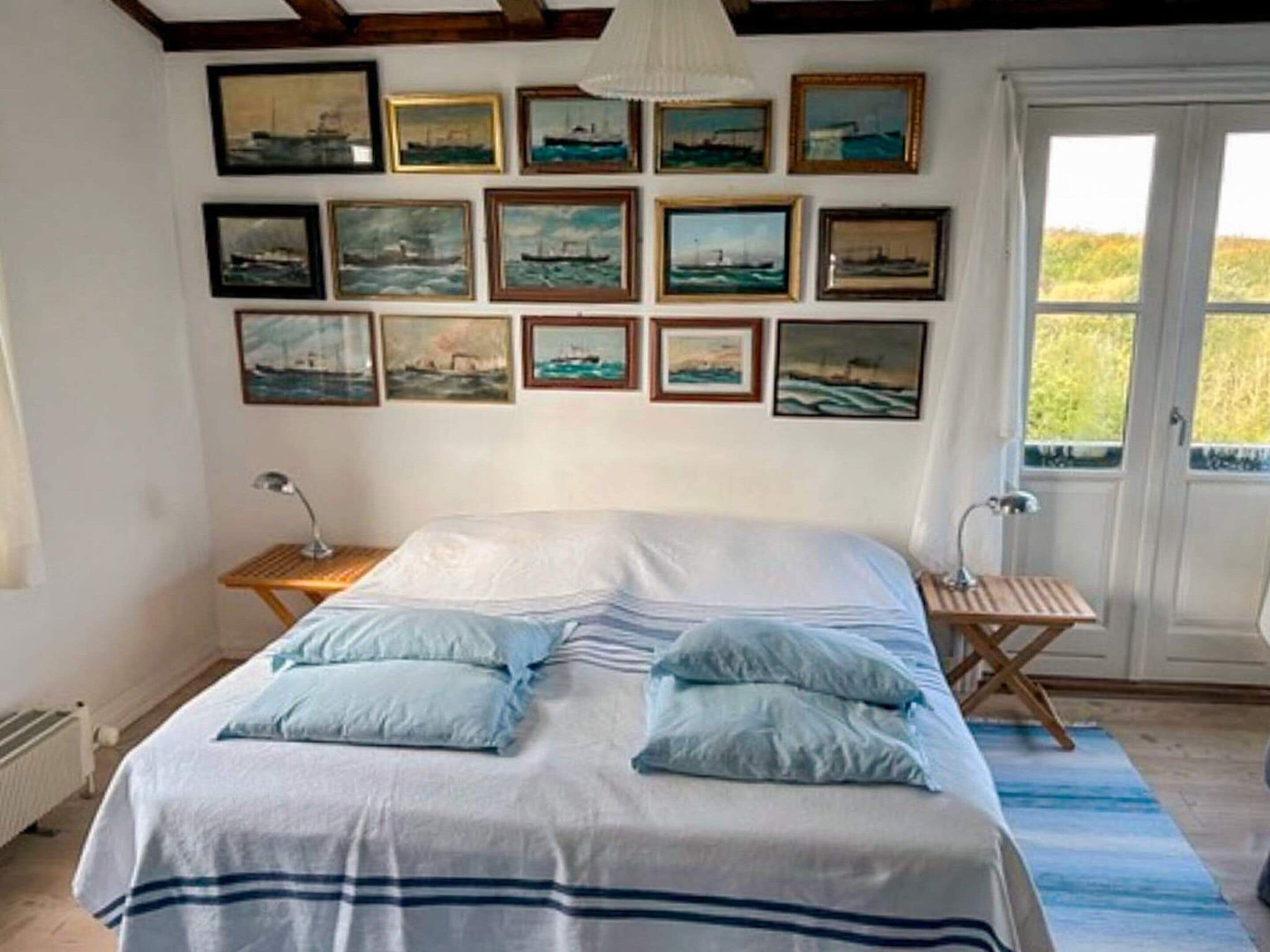 Un dormitorio con cama, almohadas, una mesita de noche, una lámpara y un ventanal con vistas.