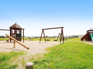A playground with swings, a slide, and a small wooden structure. - 4 Star Holiday Home in Brovst (Brovst)