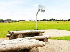 A basketball court with a metal hoop, wooden benches, and a grassy field.