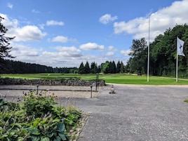 Un camino pavimentado que conduce a un campo de golf, con un muro de piedra y plantas a la izquierda.
