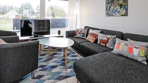 A modern living room with a flat-screen TV, grey sofas, patterned cushions, a coffee table, and a painting on the wall. - 4 Star Holiday Home in Brovst (Brovst)