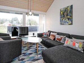 A modern living room with a flat-screen TV, grey sofas, patterned cushions, a coffee table, and a painting on the wall. - 4 Star Holiday Home in Brovst (Brovst)