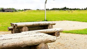 A basketball court with a metal hoop, surrounded by a grassy field and wooden benches. - 4 Star Holiday Home in Brovst (Brovst)