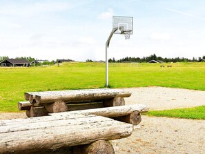 A basketball court with a metal hoop, surrounded by a grassy field and wooden benches. - 4 Star Holiday Home in Brovst (Brovst)