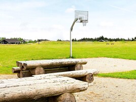 Una cancha de baloncesto con aro metálico, rodeada de un campo de césped y bancos de madera.