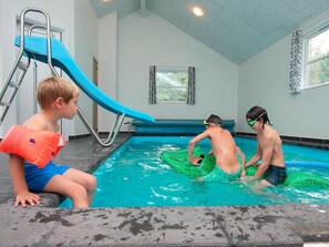 An indoor swimming pool with a blue slide, a ladder, and a window with curtains. - Spacious Holiday Home in Blavand Denmark With Sauna (Blavand)