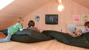 Een kamer met houten wanden en een schuine hemel, met een aan de muur bevestigde televisie en een klein tafeltje.