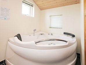 A modern bathroom with a freestanding bathtub, a window, and a wooden ceiling.