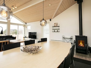 A modern living room with a large wooden dining table, a TV, a fireplace, and pendant lighting.