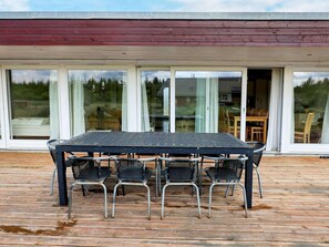 Une terrasse en bois avec une table et des chaises, de grandes portes vitrées et une vue sur l’extérieur.