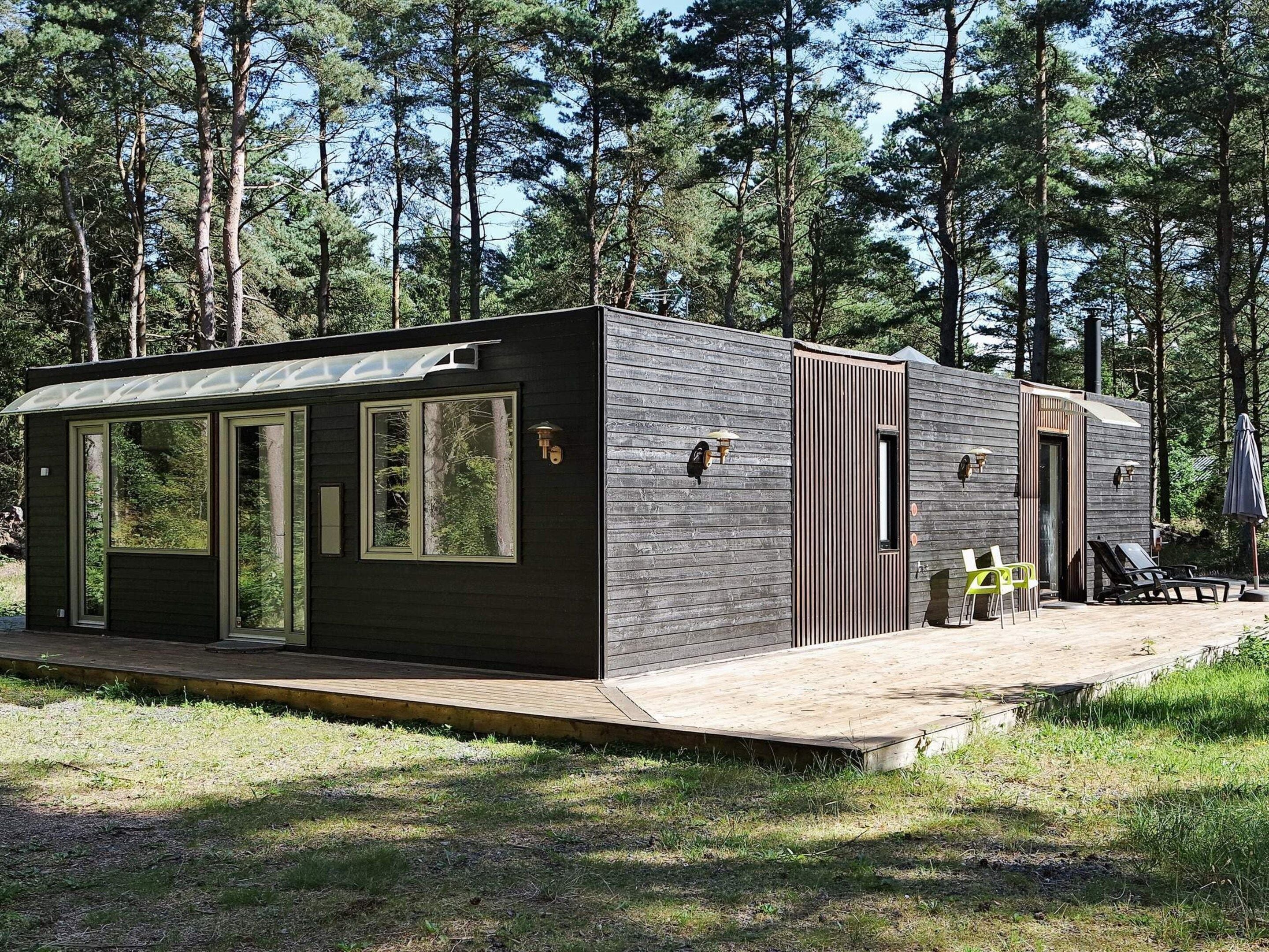 Una cabaña pequeña con terraza, ventanas amplias y una puerta.