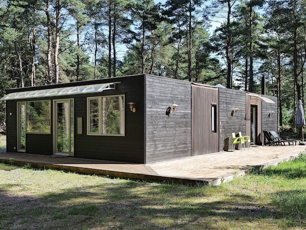 Una cabaña pequeña con terraza, ventanas amplias y una puerta.