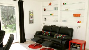 A modern living room with a leather sofa, red ottoman, and a red side table.