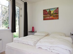 Un dormitorio con cama, una ventana con cortinas, un cuadro en la pared y una mesita de noche con un florero.