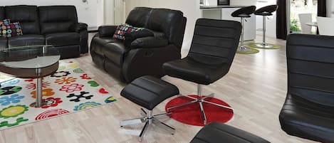Un salon moderne avec un canapé, des fauteuils, une table basse et une cuisine en arrière-plan.