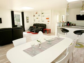 A modern living room with a black sofa, a dining table with chairs, and a kitchen area with a sink and cabinets. - 5 Star Holiday Home in Hadsund (Hadsund)