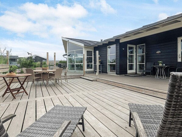 A wooden deck with outdoor furniture, including a table and chairs, and a glass door leading to a covered area.