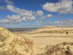 Kustlandschap met duinen, een vuurtoren en een persoon die op het strand staat.