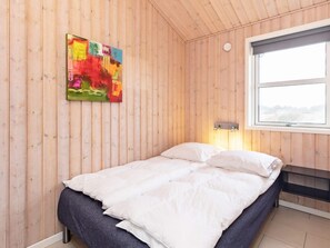 Ein Schlafzimmer mit Holzwandverkleidung, einem Bett mit weißer Bettwäsche, einem farbenfrohen abstrakten Gemälde und einem Fenster mit Blick auf eine verschneite Landschaft.
