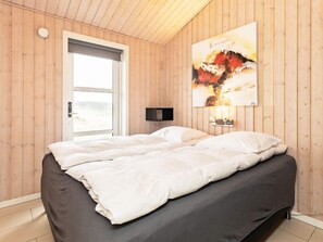 A bedroom with a bed, a door, a window, and a wall-mounted artwork.