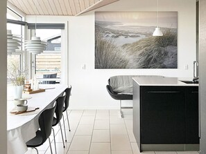 A modern kitchen with a dining area, featuring a large window, a pendant light, and a wall-mounted artwork.