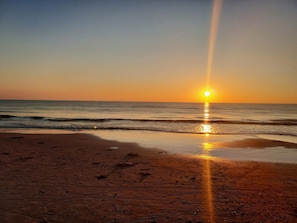 Ein Strand mit Sonnenuntergang, Wellen und wolkenlosem Himmel.