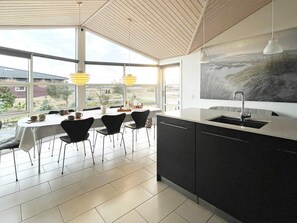 A modern kitchen with a large island, a dining area with chairs and a table, and a view of the outdoors.