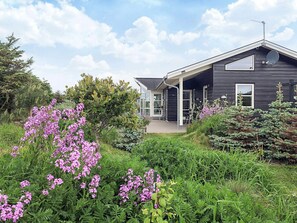 Ein modernes Haus mit überdachter Veranda, umgeben von üppigem Grün und blühenden Pflanzen.