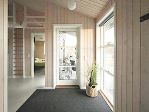 A hallway with a wooden door, a potted plant, and a view of a room with a bed. - 5 Star Holiday Home in Lokken (Lokken)