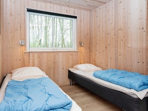 A room with two beds, wooden walls, a window with a view of trees, and a wall-mounted light fixture. - 5 Star Holiday Home in Nordborg (Nordborg)