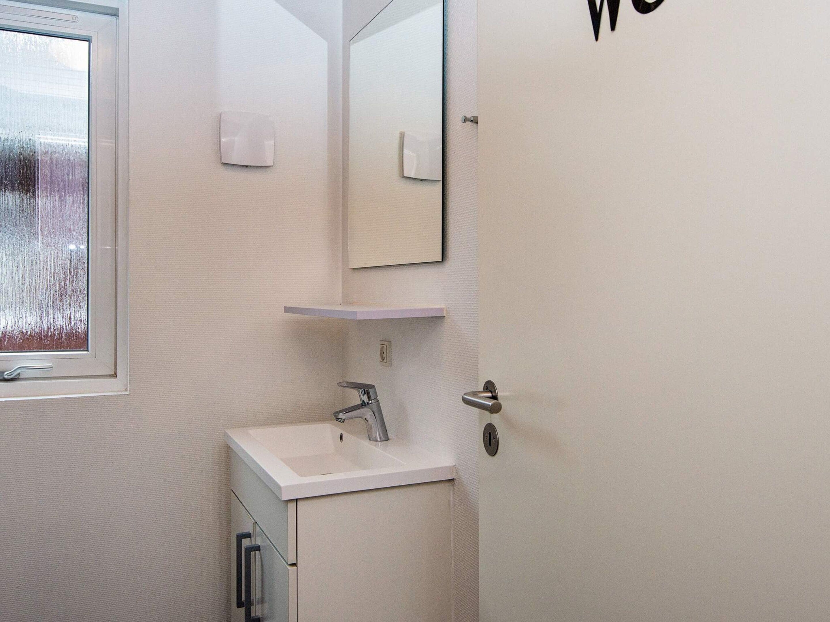 Ein Badezimmer mit einem weißen Waschbecken, einem Spiegel und einer Tür mit einem 'W'-Schild.
