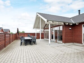 A covered patio area with a table and chairs, a wooden fence, and a view of neighboring houses. - 5 Star Holiday Home in Nordborg (Nordborg)