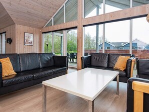 A modern interior with a wooden ceiling, large windows, a black leather sofa, and a white table. - 5 Star Holiday Home in Nordborg (Nordborg)