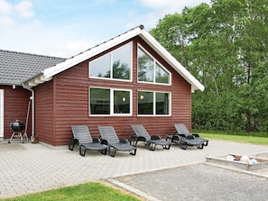 A wooden building with a sloped roof, multiple windows, and a paved area with lounge chairs. - 5 Star Holiday Home in Nordborg (Nordborg)