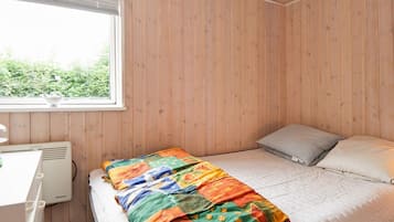 Quarto com parede de madeira, cama com manta colorida, travesseiro e janela com persianas.