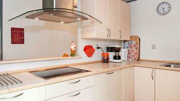 Una cocina con campana extractora de acero inoxidable, armarios de madera, cafetera y un reloj en la pared.
