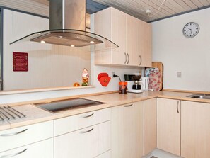 Una cocina con campana extractora de acero inoxidable, armarios de madera, cafetera y un reloj en la pared.